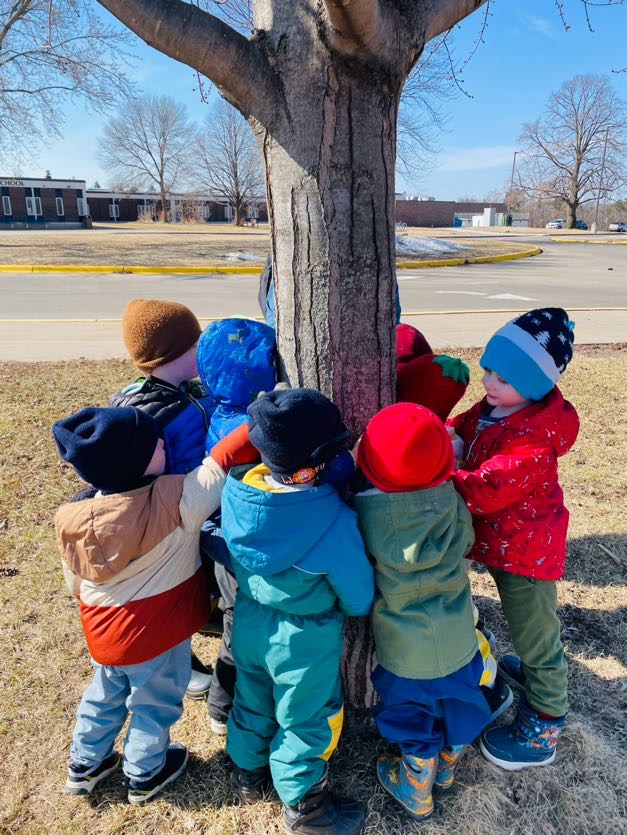 a small group of children huddle around a tree trunk
